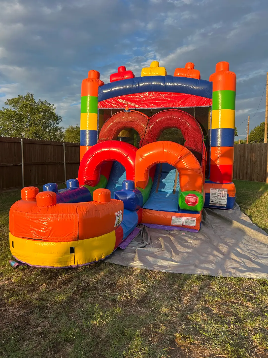 Colorful building-block bounce house combo with slide set up on a ground tarp over grass in a fenced Van Alstyne, TX yard