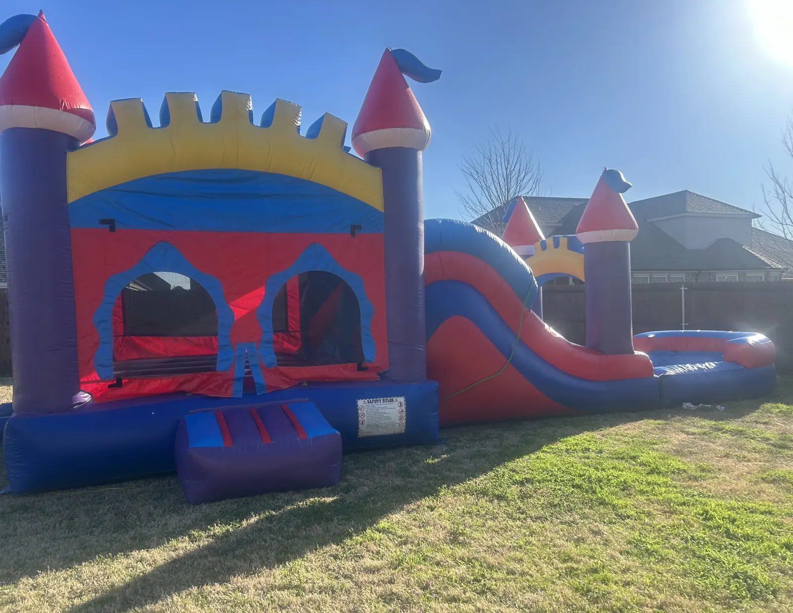 Castle bounce house combo with a slide set up on a lawn beside a wood privacy fence in Melissa, TX