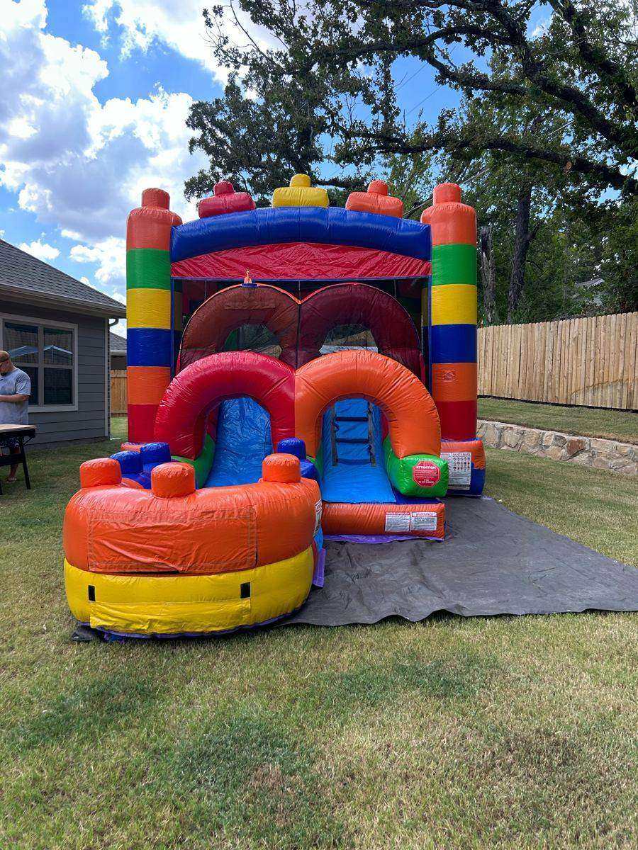 Colorful building-block bounce house combo with slide set up on a ground tarp over grass in Howe, TX