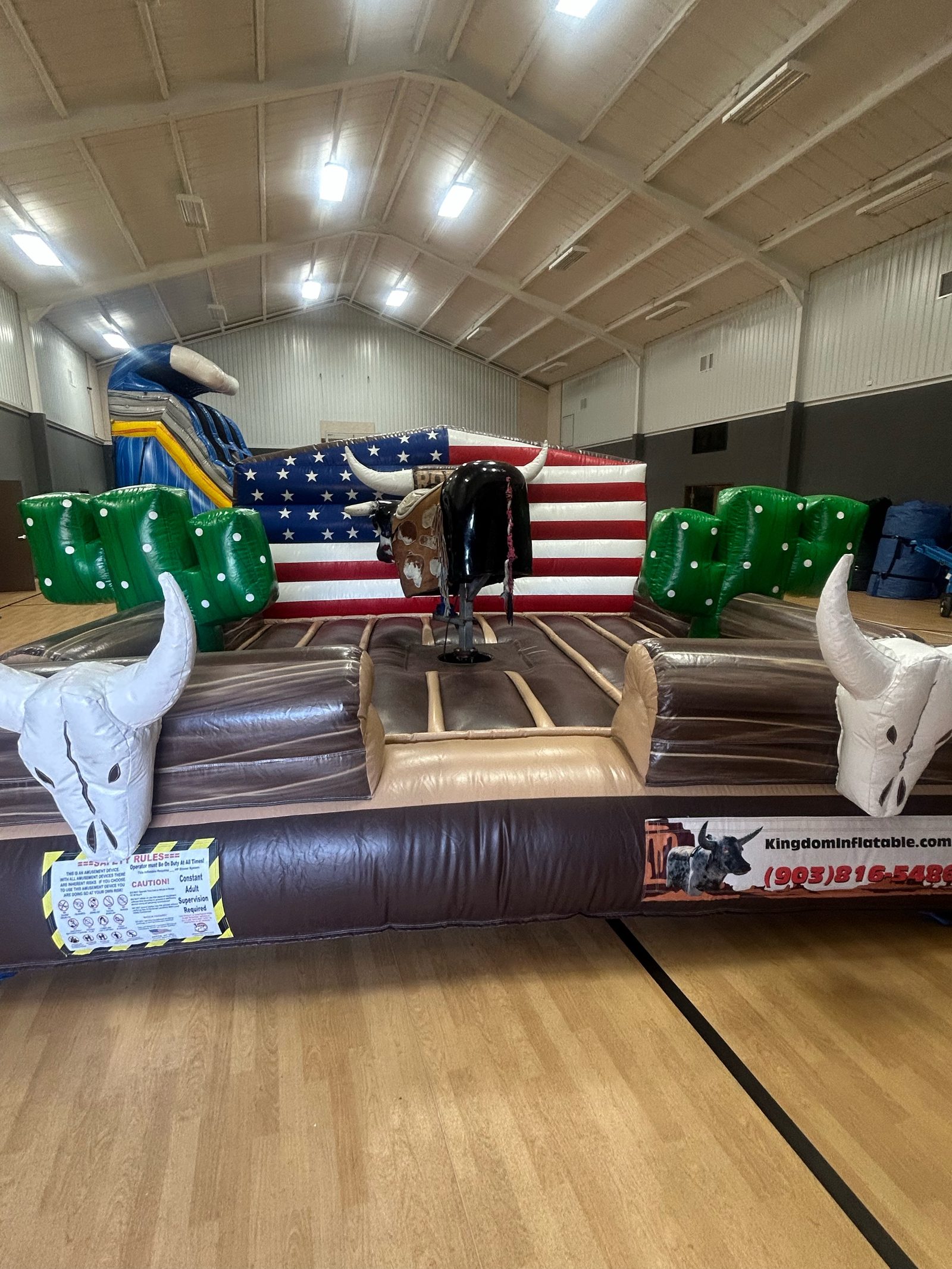 American flag mechanical bull inflatable with cactus and longhorn skull pillars, set up on a gym floor in Howe, TX