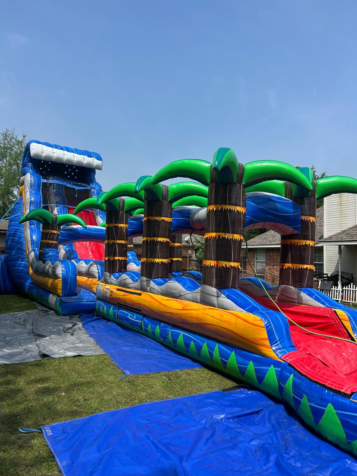 Ultra Tropical Wave water slide with palm-tree arches set up on grass in Pottsboro, TX