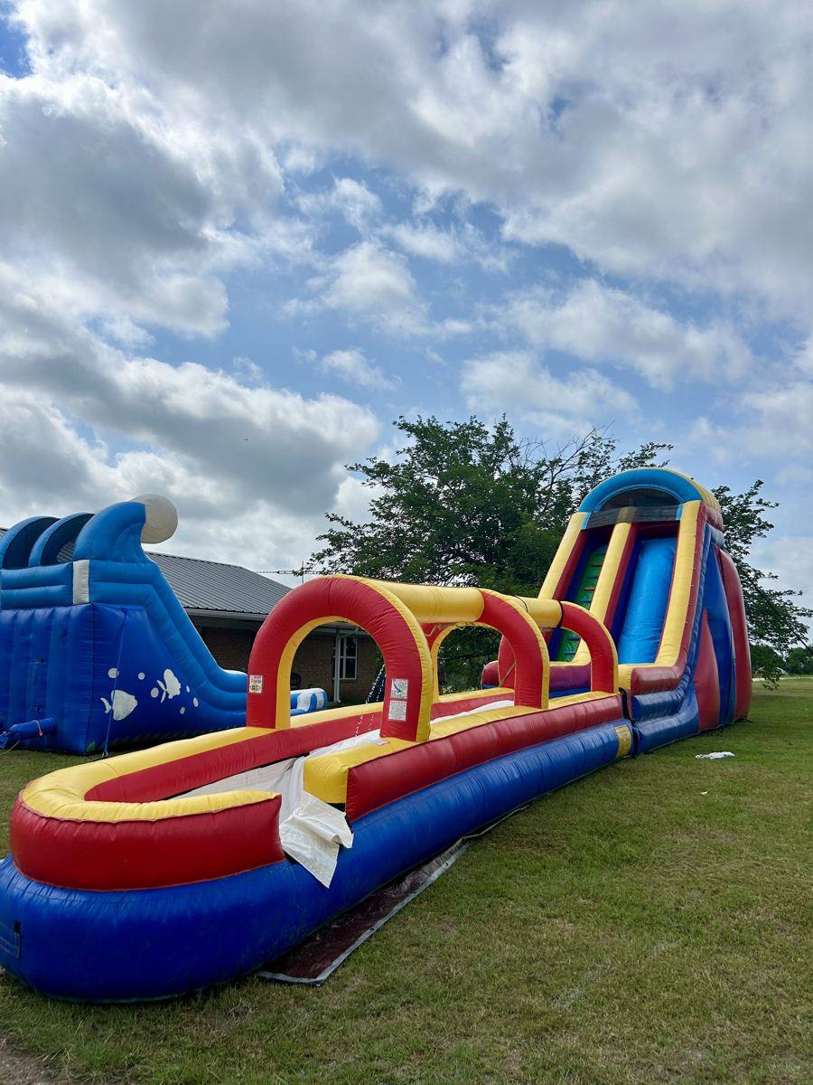 Dual-lane inflatable slip and slide with a red and yellow splash lane set up on grass in Van Alstyne, TX