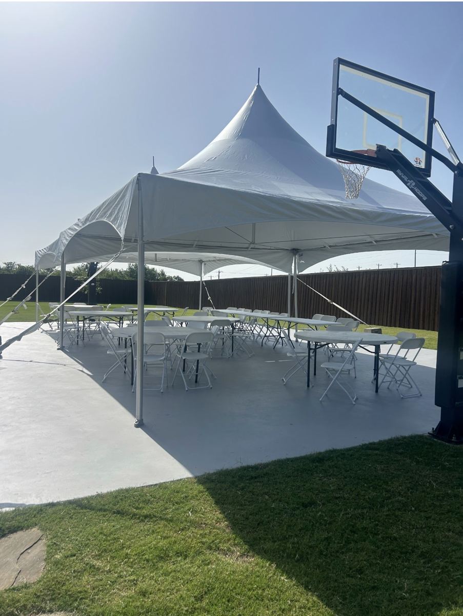 Close view of a white high-peak party tent with rows of tables and chairs on a backyard sport court in Van Alstyne, TX