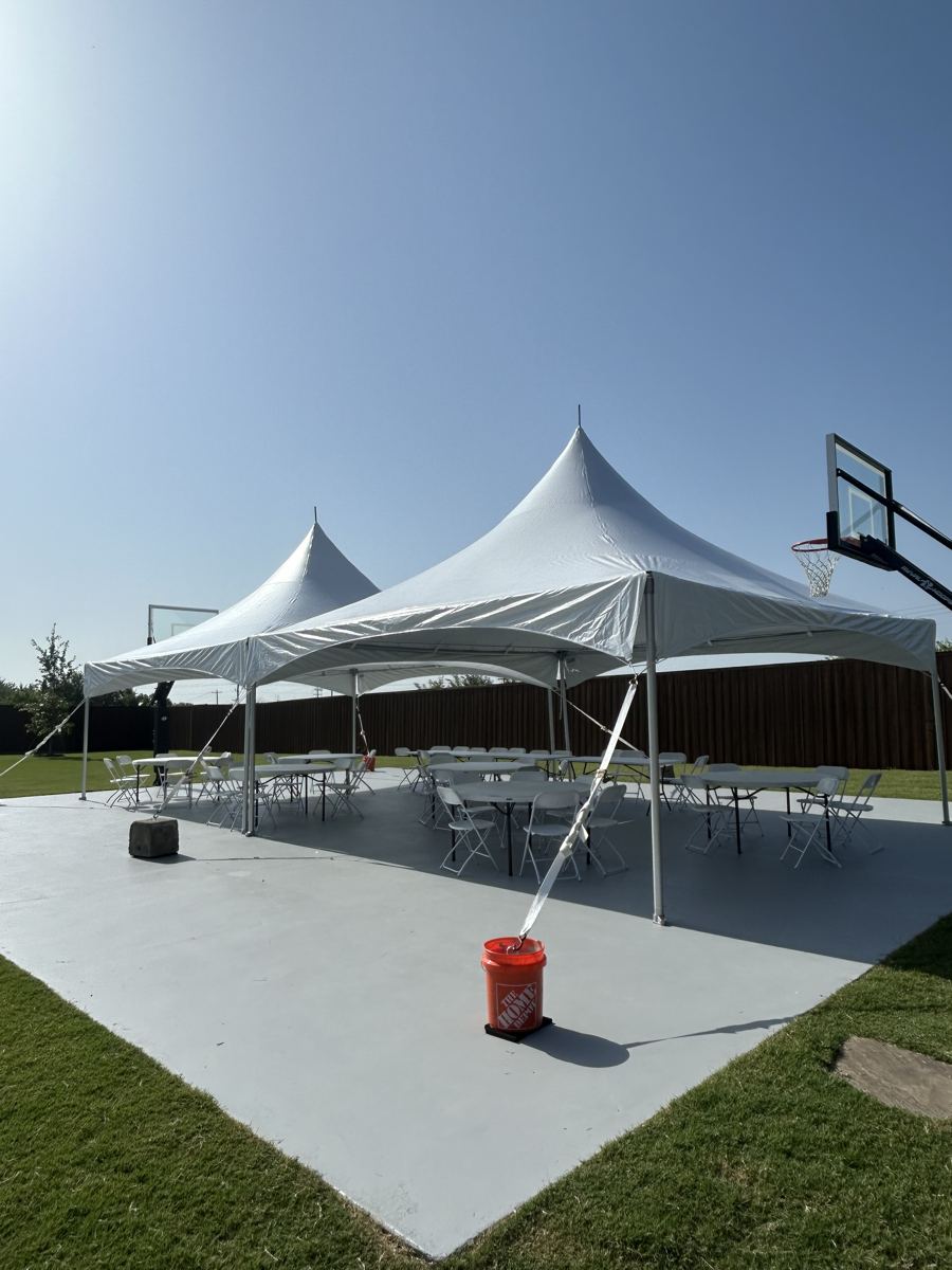 Two white high-peak party tents with tables and chairs set up on a concrete sport court beside a lawn in Van Alstyne, TX