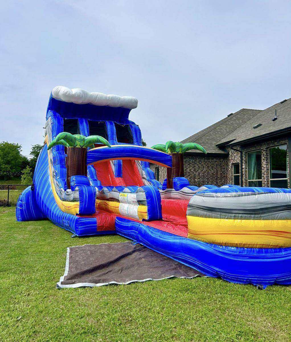 Tall tropical inflatable water slide with palm trees set up on grass with a ground tarp in a Van Alstyne, TX backyard